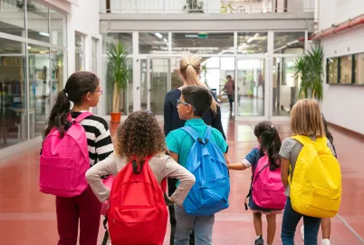 Crianças com bolsas escolares coloridas entrando na escola com controle de acesso
